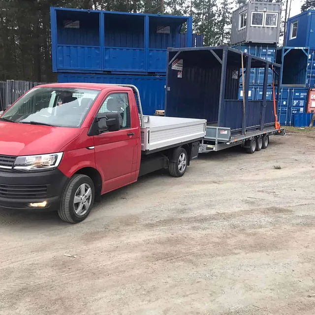 Rød varebil trekker tilhenger med blå gangtunnel, omgitt av containere.
