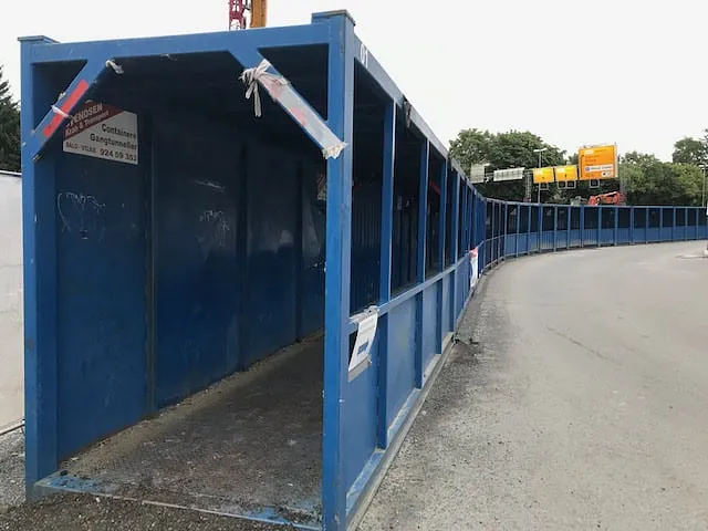 Lang blå gangtunnel i stål svinger langs en asfaltvei ved anleggsområde.