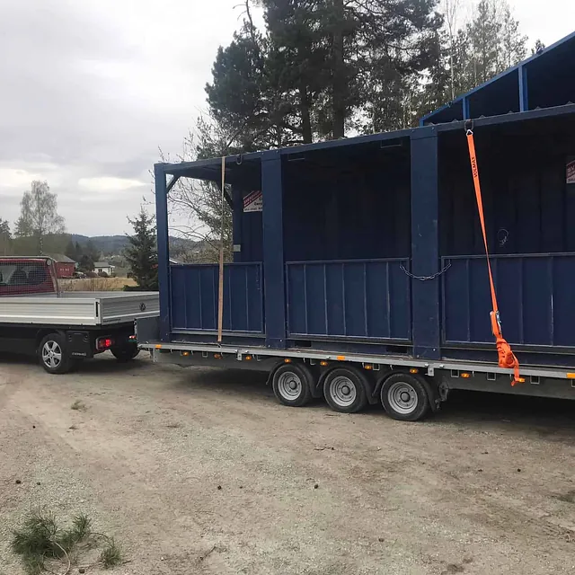 Rød varebil med henger transporterer to blå gangtunneler i stål.