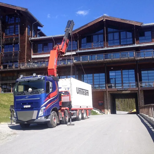 Kranbil foran stort hotellbygg løfter hvit container merket "Unileam" ved innkjøringsport.