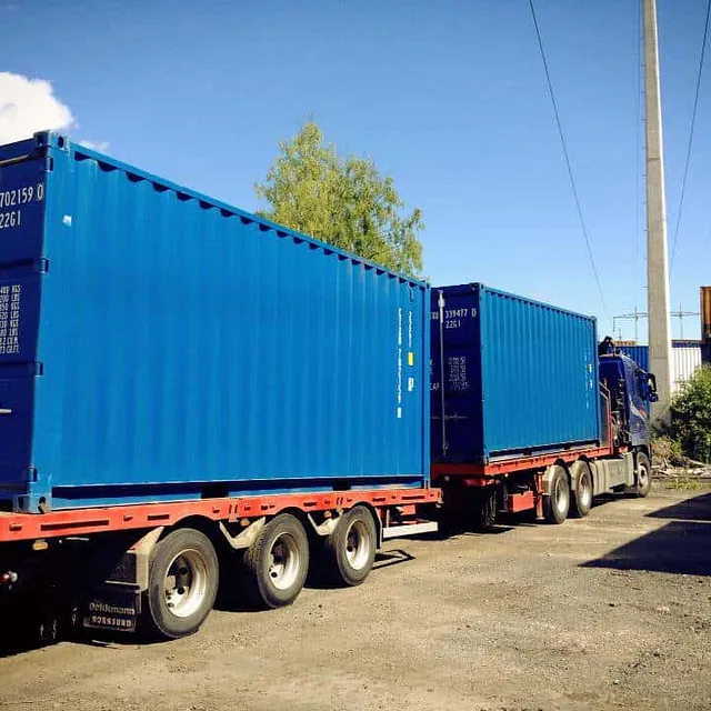Lastebil med to blå containere på henger kjører ut fra containerområde.